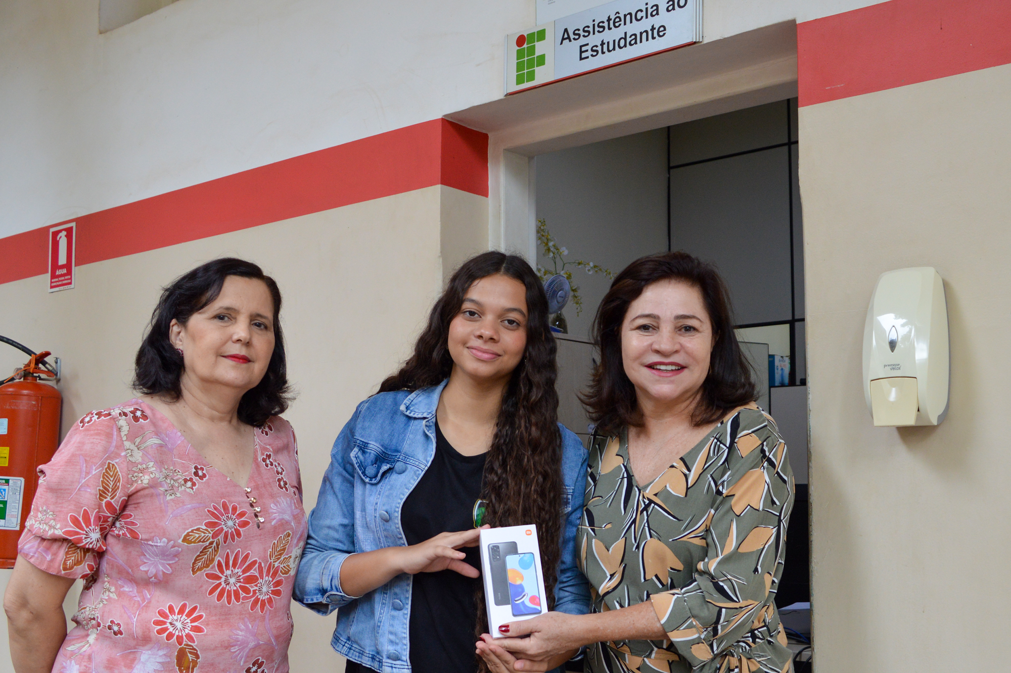 Vycctoria Gabrielly, aluna do curso de Controle Ambiental, recebe celular ao lado de Cristina Hidalgo (coordenadora de Assistência Estudantil) e Adriana Ferreira (diretora-geral)